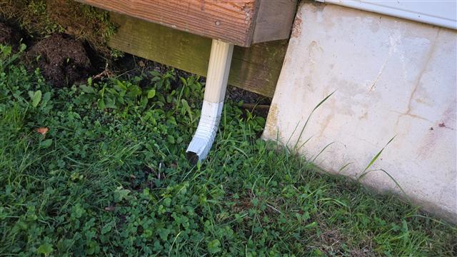 Short downspout outlet ending beside the foundation and vegetation.
