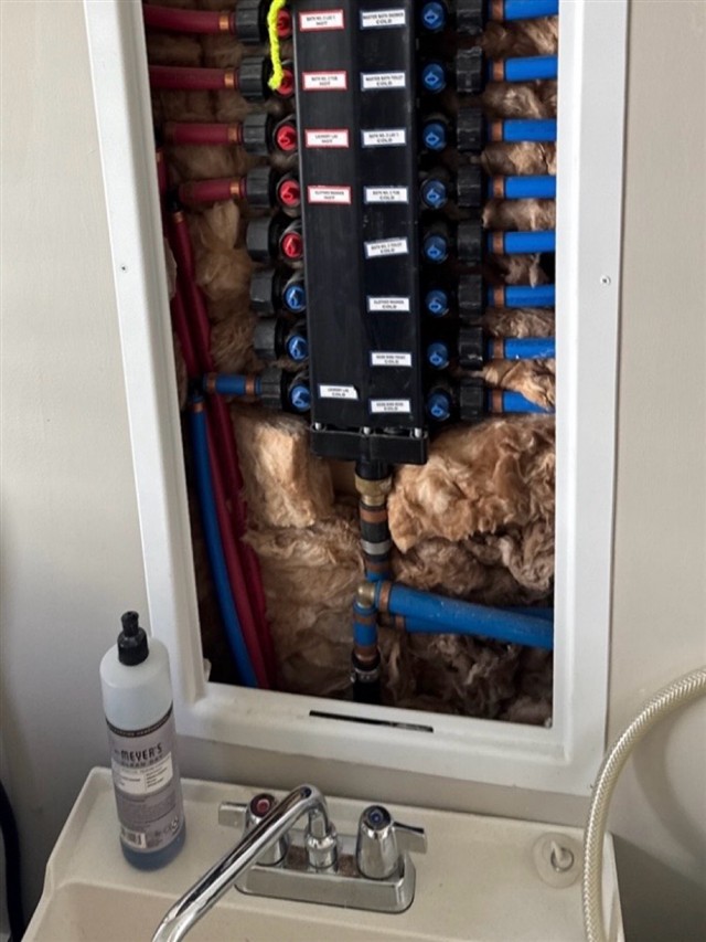 Original TMK inspection photograph of a water-distribution manifold and connected piping above a utility sink, documenting a supply-piping alteration noted in the report.
