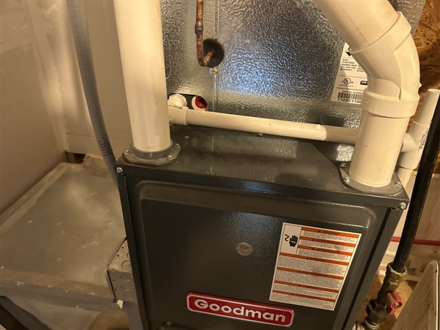 Original TMK inspection photograph showing the top of a furnace cabinet, the evaporator-coil cabinet above it, and adjacent white piping.